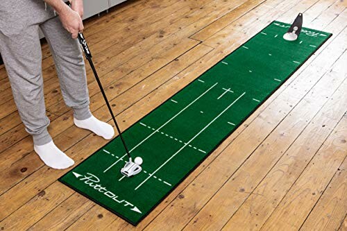 Person using an indoor golf putting mat on wooden floor.